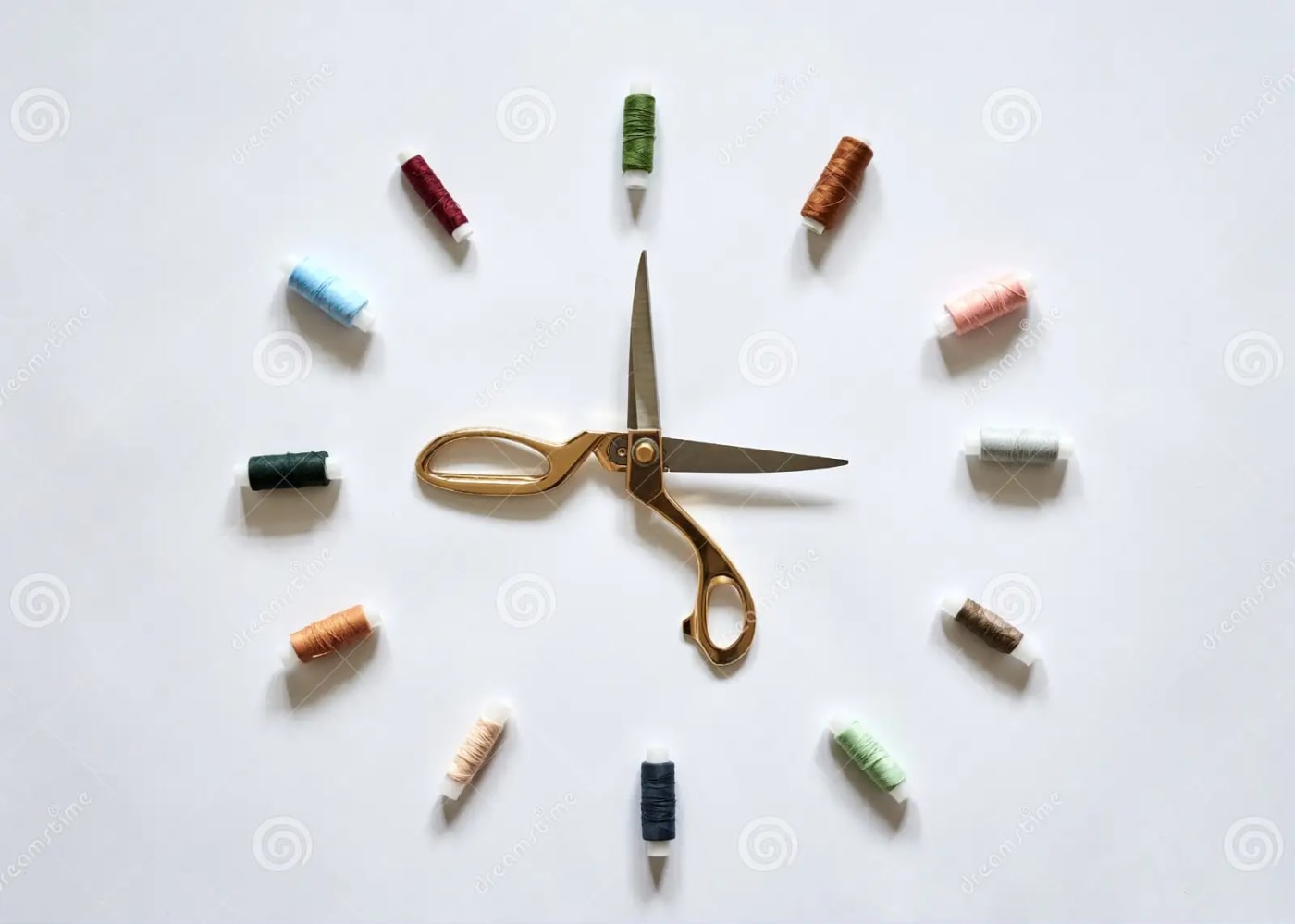Relógio formado por retróses de linha (números) dispostos de forma circular ao redor de uma tesoura aberta (ponteiros) em fundo branco simbolizando costura e pontualidade.