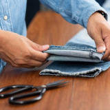 Uma pessoa cortando uma bainha de calça jeans, ajustando o comprimento da peça de roupa com cuidado e precisão.